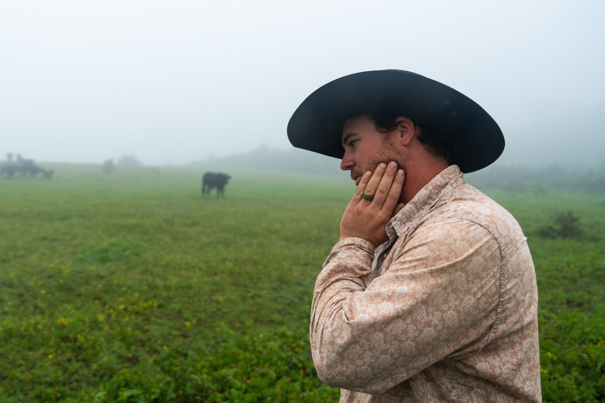 Hawaiian rancher Daniel Jacintho stands in fog with his hand on his face.